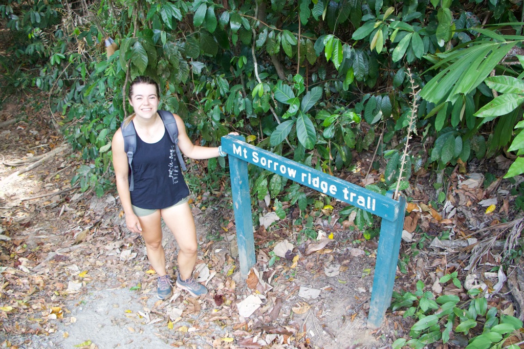 Sarah standing at the entrance sign for the Mt Sorrow ridge trail.